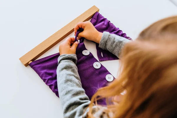 Girl buttoning a montessori frame to develop the dexterity of he Royalty Free Stock Photos