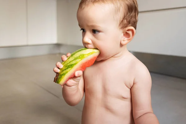 Bebé de 10 meses de edad, sentado en el suelo de su cocina mordisqueando un — Foto de Stock