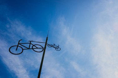 Bir kutup üzerinde asılı Bisiklet siluetleri ile heykel, gökyüzü bir