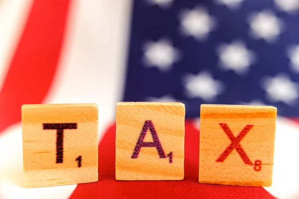 Word Tax sullo sfondo sfocato di una bandiera americana . — Foto Stock