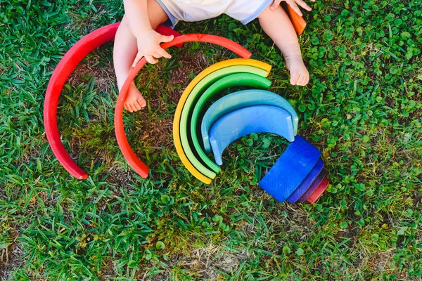 Baby spielt mit einem bunten hölzernen Regenbogen auf dem Gras, Kind — Stockfoto