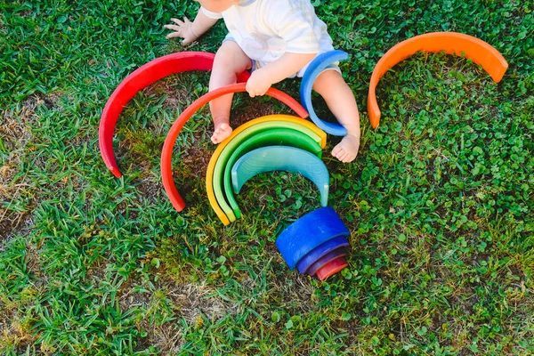 Baby spielt mit einem bunten hölzernen Regenbogen auf dem Gras, Kind — Stockfoto