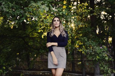 Sonbaharda ağaç yapraklarıyla çevrili zarif siyah beyaz elbisesiyle kameraya bakan güzel bir genç kadının portresi..