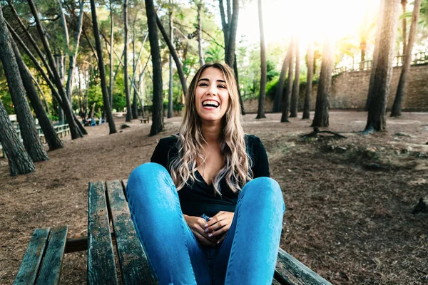 Engraçado rindo jovem mulher sentada em uma mesa de madeira em um parque . — Fotografia de Stock