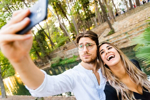 Enamorados abrazándose mientras se toman una selfie entre risas — Foto de Stock