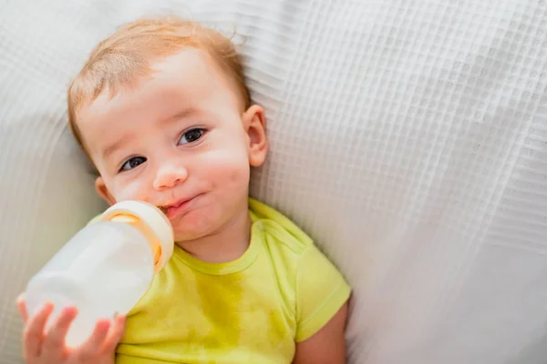 Baby taking his bottle of milk on a sofa with a funny and hungry — Stock Photo, Image