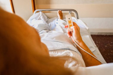 Sick woman in bed pressing the remote bell to request assistance