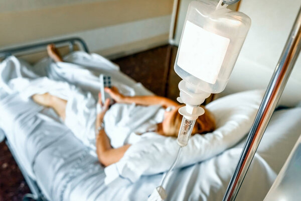  Saline solution drip  bag hanging on the bed of a sick woman.