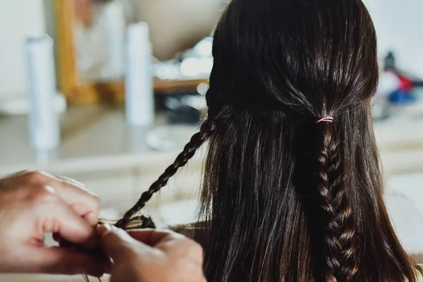 A hairdresser makes braids in the hair of a brunette woman. — Stock Photo, Image