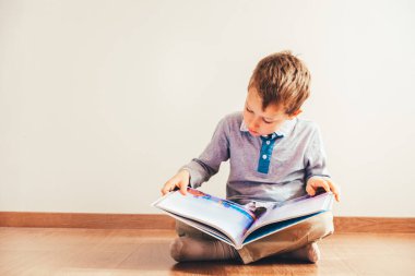 Beyaz arka plan üzerinde izole dizlerinin üzerine bir kitap okuma ile katta oturan çocuk.