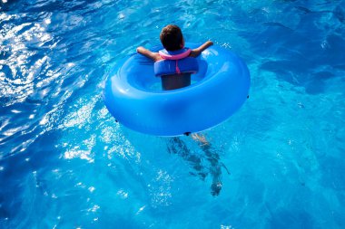 Havuzda banyo yapan bir çocuk büyük yuvarlak bir şamandırayla oynuyor..