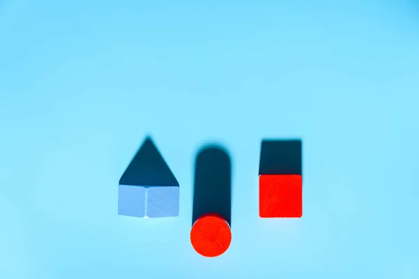 Three geometric figures of solid colors illuminated with hard light on simple blue background.