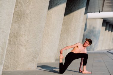 Genç adam şehrin stresinden kurtulmak ve egzersiz yapmak için yoga yapıyor..