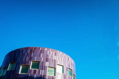Mavi fayanslı alışılmadık yuvarlak bina modern mimarinin bir örneği, arka planda bol yer ve mavi gökyüzü var..
