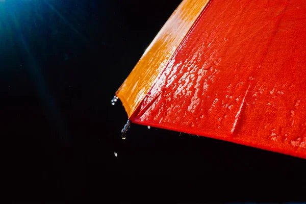 Rain on a warm-toned umbrella lit by the sun, isolated on black background with copy space.