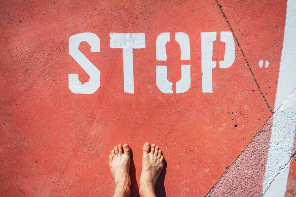 An illegal immigrant stands barefoot at a stop sign on the ground.