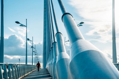 Endüstriyel bir köprüde büyük sütunlar ve kablolar ile yürüyen kişi.