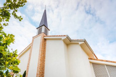 Pürüzsüz beyaz duvarları ve bulutlu bir arkaplanı olan Protestan kilisesi cephesi.