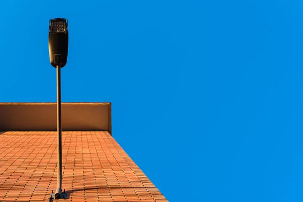 Lámpaoszlop Egy Épület Vörös Falán Nappal Kék Háttérrel — Stock Fotó