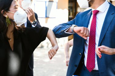 İki insan selamlaşırken dirseklerine dokunur, maske takar.
