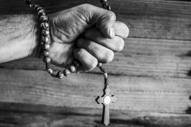 Dindar bir insanın eli, duaları sırasında Hıristiyan tespihi tutar. Siyah beyaz ormanların odaklanmamış arka planı..