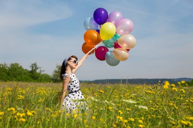 Beyaz rockabilly nokta elbise ve çayır bir sürü renkli balon ile genç bir kadın