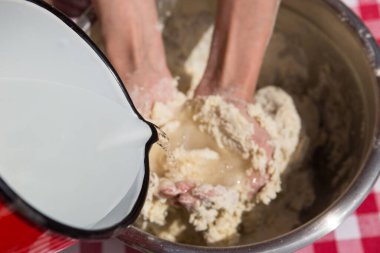 Kadın hamuru yoğuruyor, kırmızı beyaz masa örtüsü.