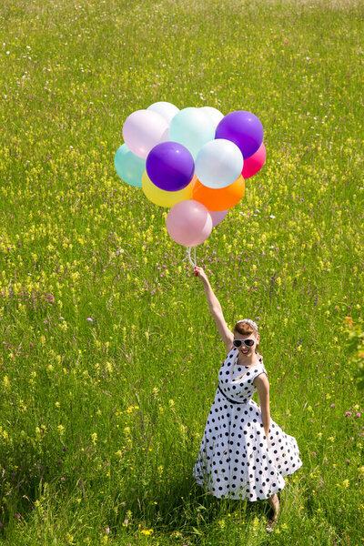 Pinup Girl with a white dotted petticoat dress and colorful balloons on the meadow, topview 