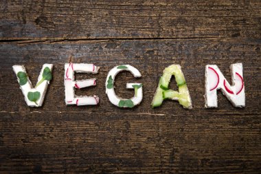 Sağlıklı sebze kanepelerinin harfleri eski ahşap bir masada Vegan kelimesini oluşturur.