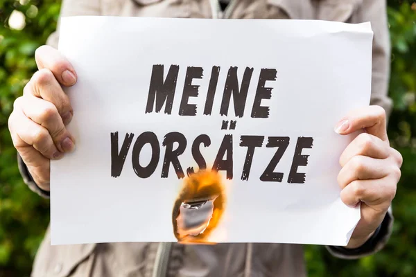 女人手里拿着一张德国文的燃烧的纸 意思是我的决心 — 图库照片