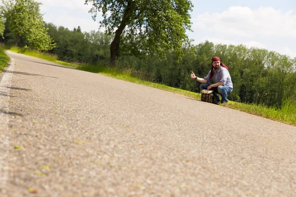 Mężczyzna Autostopowicz Siedzi Ulicy Trzymając Kciuk Górze — Zdjęcie stockowe