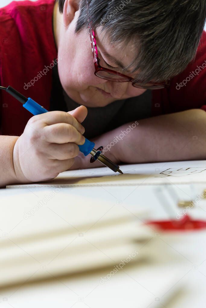 mentally disabled woman is doing woodburning as art therapy, vertical