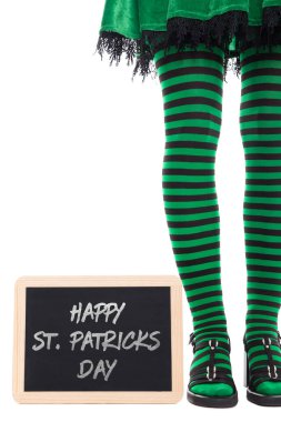 Siyah ve yeşil çizgili bacaklar Leprikan bir kızdan Mutlu Patrick Günü yazılı bir yazı tahtası.