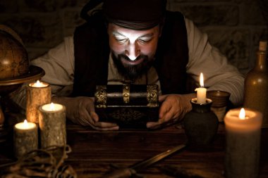 Bir korsan, avıyla birlikte eski bir tahta kutuya bakıyor. 