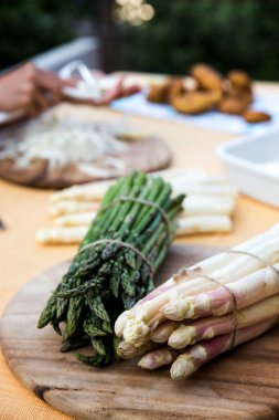 Masadaki beyaz ve yeşil kuşkonmaz ve yeni patatesler. Kadın kuşkonmazı soyuyor.