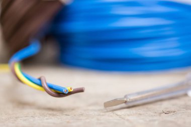 Tahta bir masada farklı elektrik kabloları, test lambası ile yakın plan.