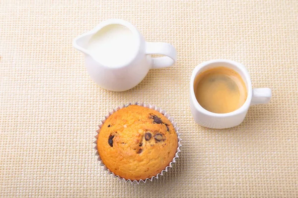 Perfect ontbijt met heerlijke zelfgemaakte cupcakes met rozijnen, chocolade chips, espressokoffie in witte kop en melk op textiel achtergrond. Muffins. — Stockfoto