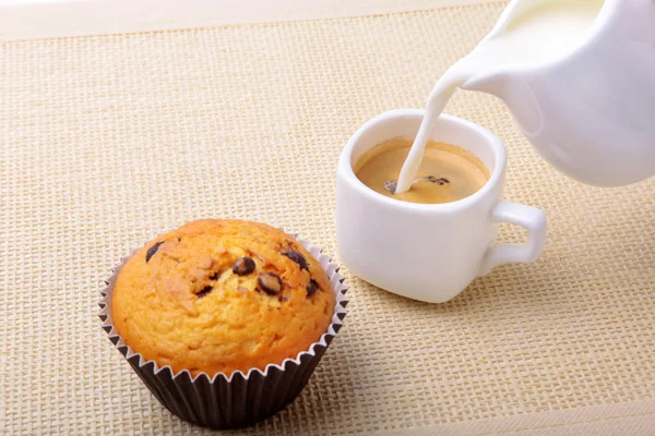 Прекрасный утренний завтрак с вкусными домашними кексами с изюмом, шоколадной стружкой, кофе эспрессо в белой чашке и молоком на текстильном фоне. Кексы . — стоковое фото