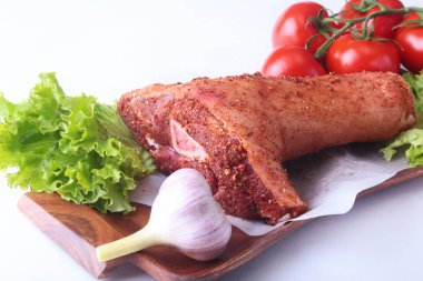 Çiğ domuz knuckle ve sebze, sarımsak, domates baharat ve marul yaprakları bir kesme tahtası üzerinde. Seçici odak. Hazır yemek pişirmek için.