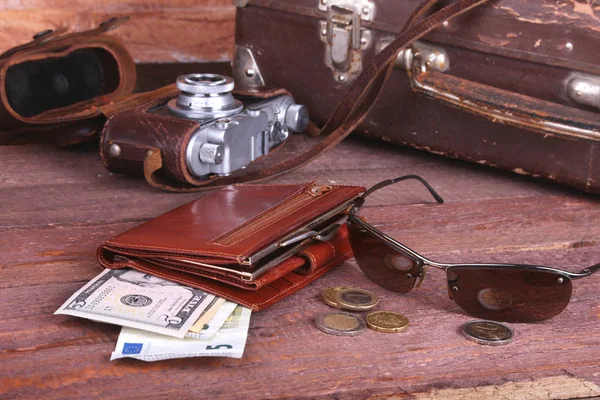 Travel concept with Vintage suitcase, sunglasses, old camera, suede boots, case for money and passport on wooden floor.