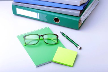 Klasörler dosyası ve modern dizüstü, kalem, gözlük ve yakınındaki beyaz bir arka plan üzerinde yalan ders kitabı ile iş yerinde tablo.