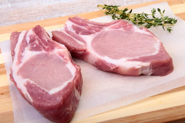 Chuletas de cerdo crudas, especias y romero en la tabla de cortar. Listo para cocinar . — Foto de Stock