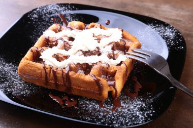 Krema, çikolata sosu ve ahududu siyah plaka üzerinde closeup ev yapımı Belçikalı Waffle. Şekerli tatlı