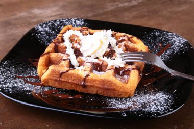 Krema, çikolata sosu ve ahududu siyah plaka üzerinde closeup ev yapımı Belçikalı Waffle. Şekerli tatlı.