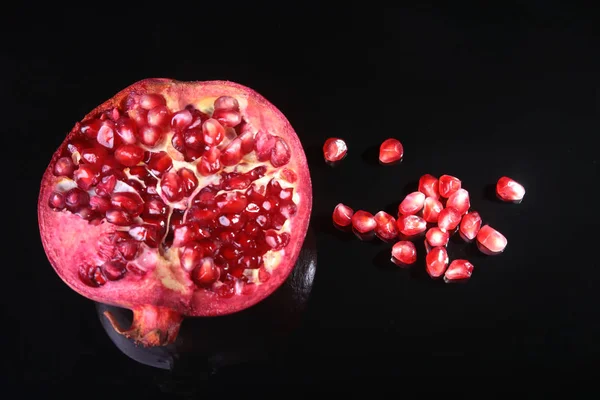 Pomegranate seeds and Beautiful ripe pomegranate on black mirror background with place for copy space. — Stock Photo, Image
