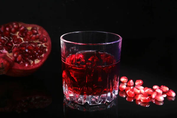 Glass with pomegranate juice Pomegranate seeds and Beautiful ripe pomegranate on black mirror background with place for copy space. — Stock Photo, Image