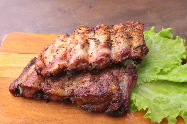 Grilled barbecued ribs with lettuce leaves, hot chili pepper and sauce on wooden cutting board. — Stock Photo, Image