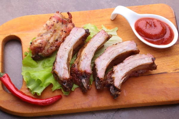 Gegrillte Rippchen vom Grill mit Salatblättern, scharfer Chilischote und Sauce auf Holzschneidebrett. — Stockfoto