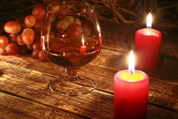 Bougies de Noël, raisins et verre avec cognac ou whisky sur fond de bois. Décoration de Noël . — Photo