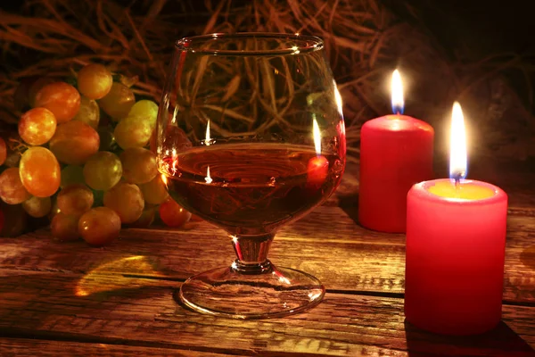 Świece, winogron i szkła z koniaku lub whisky na tle drewna. Dekorację świąteczną. — Zdjęcie stockowe